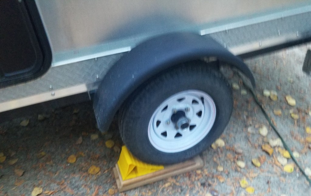 wheel of Teardrop trailer, with planks beneath and a chock in place