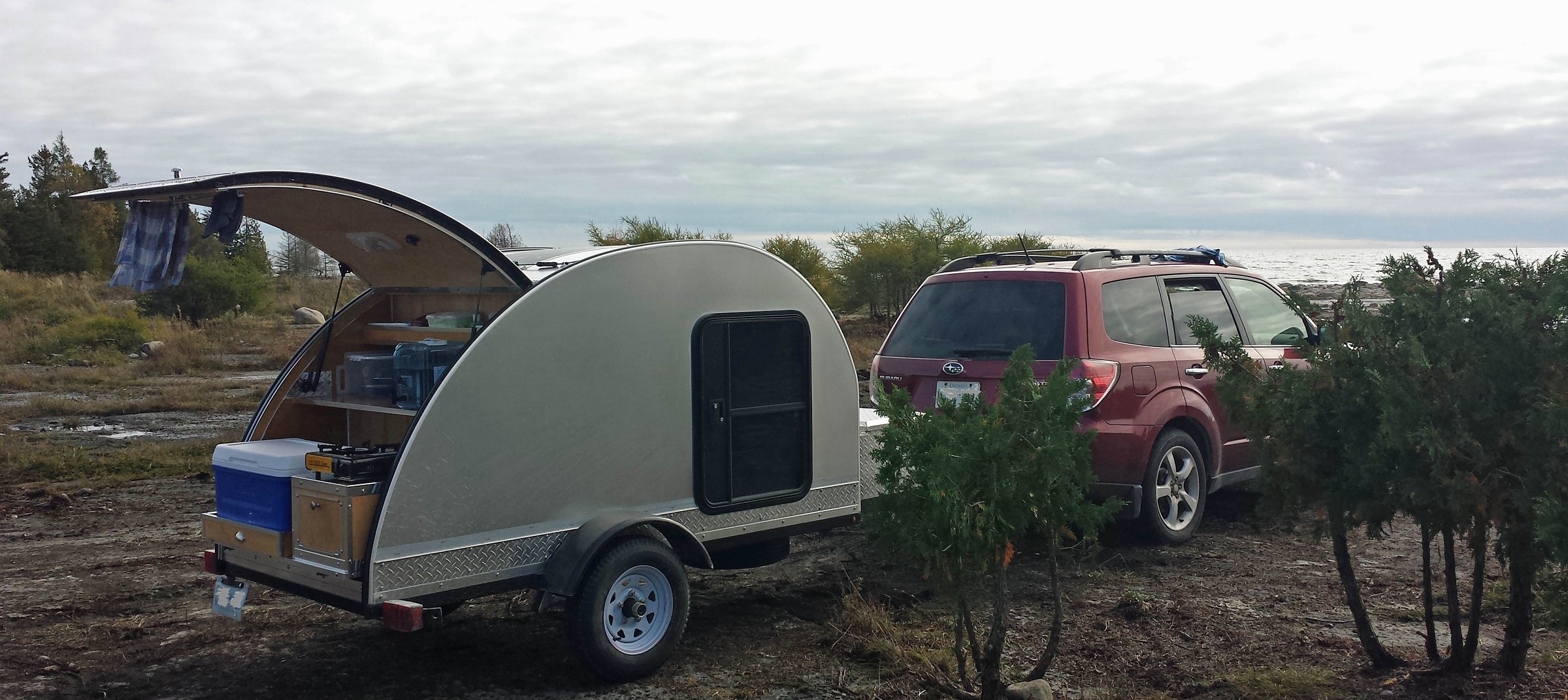 car with teardrop trailer, rear hatch open, on rough rock shore landscape