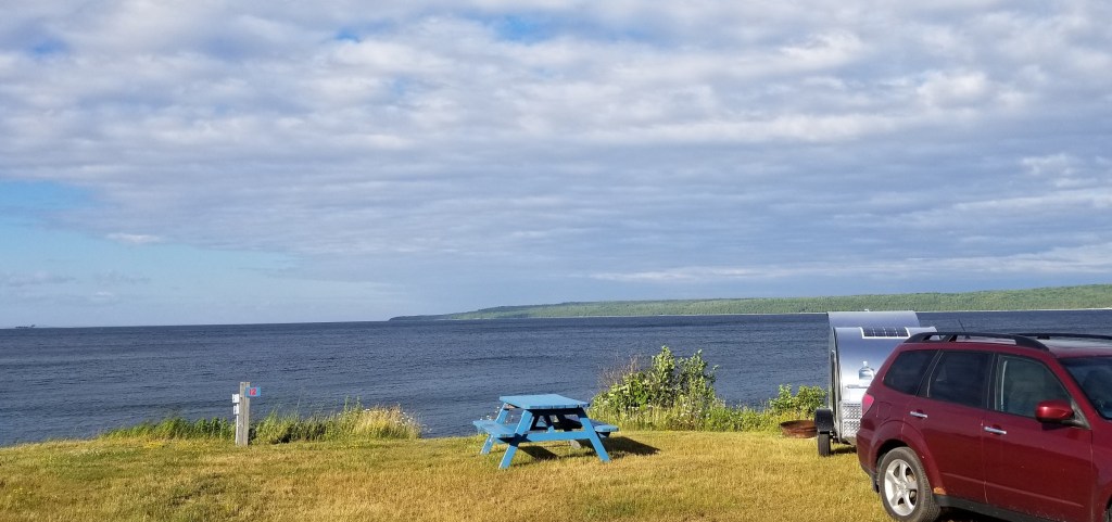 Teardrop trailer parked near shore, looking out to vast lake.