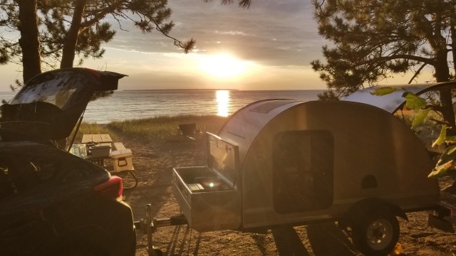 teardrop trailer set up near shore with sunset background
