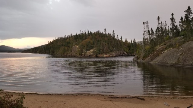 sheltered inlet with sandy shore foreground, rocky shore background